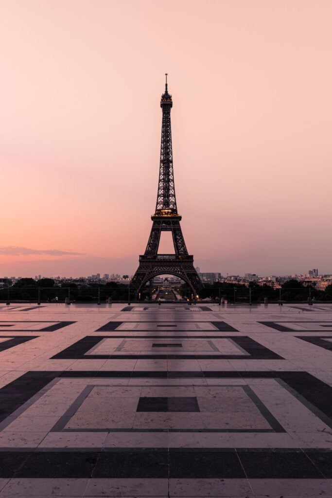 Eiffel Tower silhouette against pink sunset sky viewed from Trocadéro plaza with geometric tile patterns in foreground