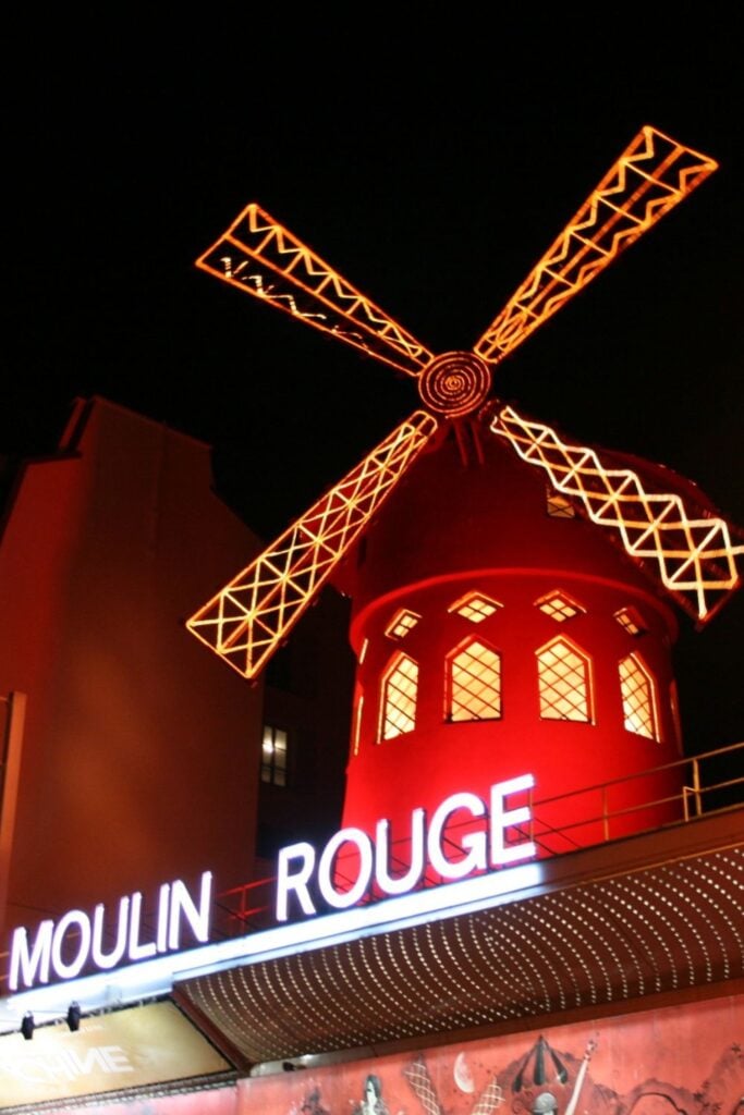 Illuminated red windmill and neon sign of the Moulin Rouge nightclub against black night sky in Paris