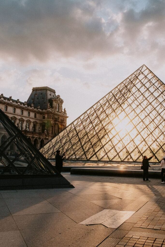 Louvre Pyramid at sunset with golden light filtering through the glass panels and historic museum buildings in background