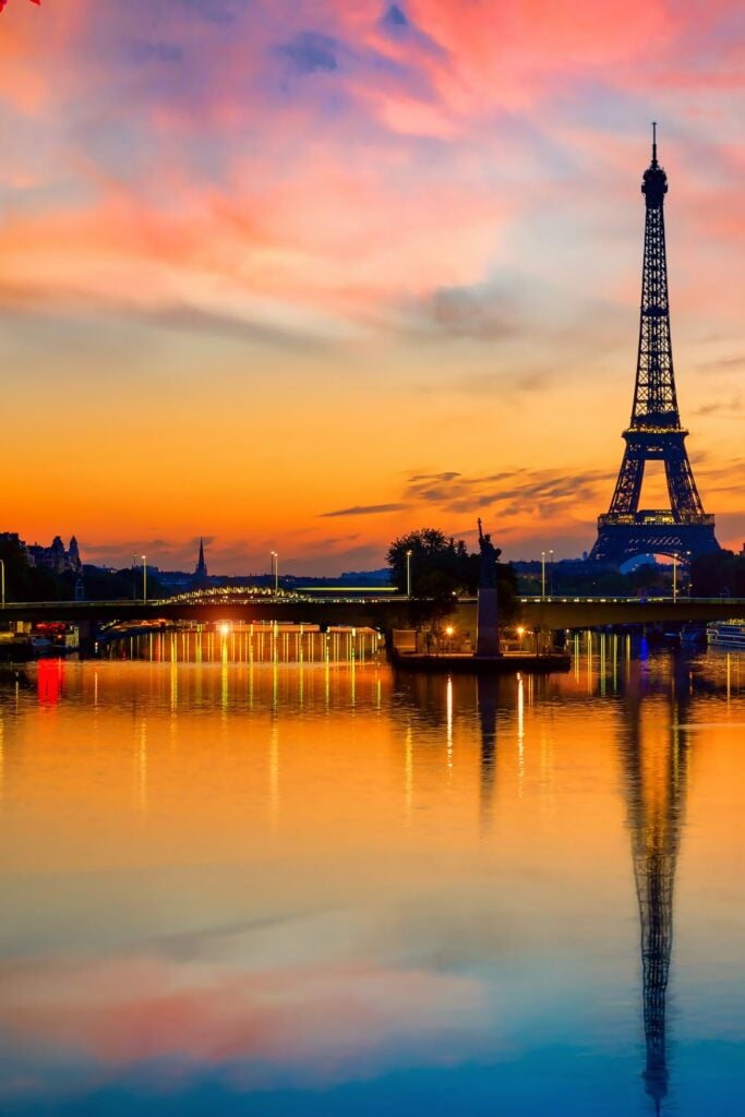 Eiffel Tower silhouette at sunset with orange and pink sky perfectly reflected in the calm Seine River waters