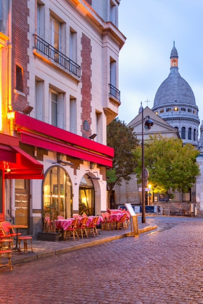 Cozy red café with outdoor seating in Montmartre with the white dome of Sacré-Cœur basilica visible in background