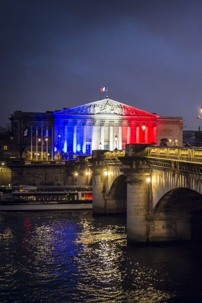 Paris Night Aesthetic: National Assembly building illuminated in blue, white and red French flag colors at night with reflections in the Seine River