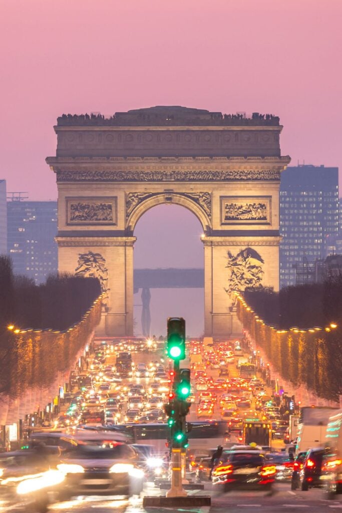 Arc de Triomphe at dusk with pink sky background and streams of car headlights on Champs-Élysées