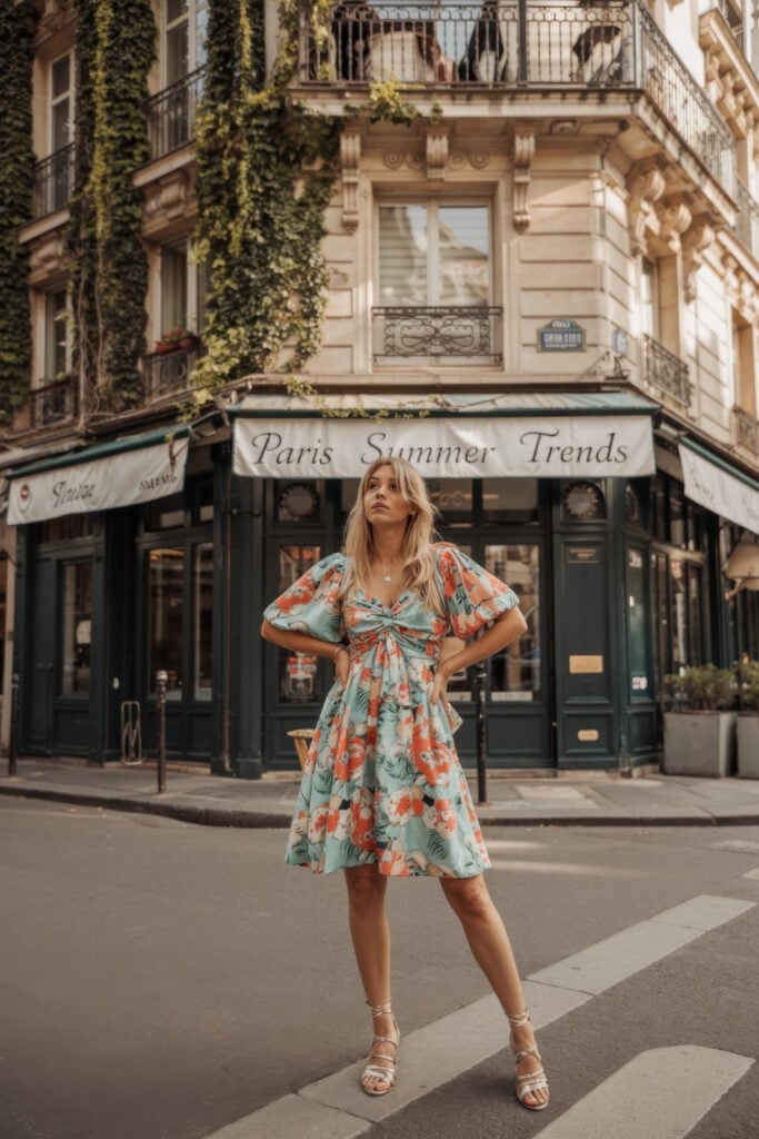 Woman in mint green and coral floral print dress with puff sleeves standing at Parisian intersection