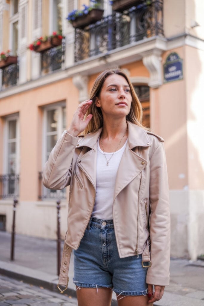 Woman wearing beige leather jacket with white t-shirt and denim shorts on Paris street