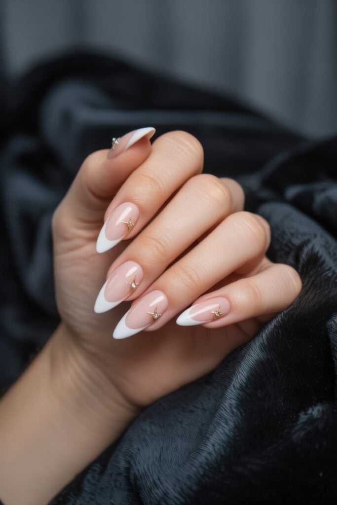 Long almond-shaped nails, white French tips, and small gold star accents photographed against dark sweater fabric.