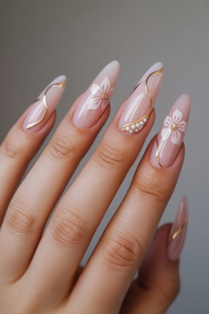 Long coffin-shaped nails with pink base, gold curved line details, white floral nail art with pearl centers, and pearl accent decorations against neutral background.