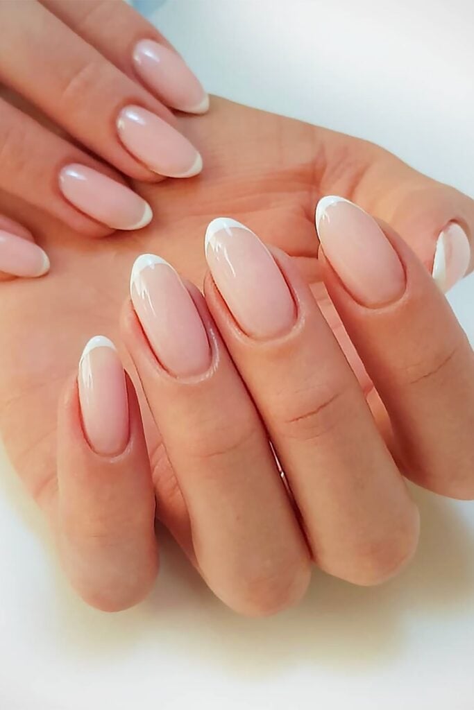 Long oval nails with milky white French tips in classic style, photographed against soft light blue background.