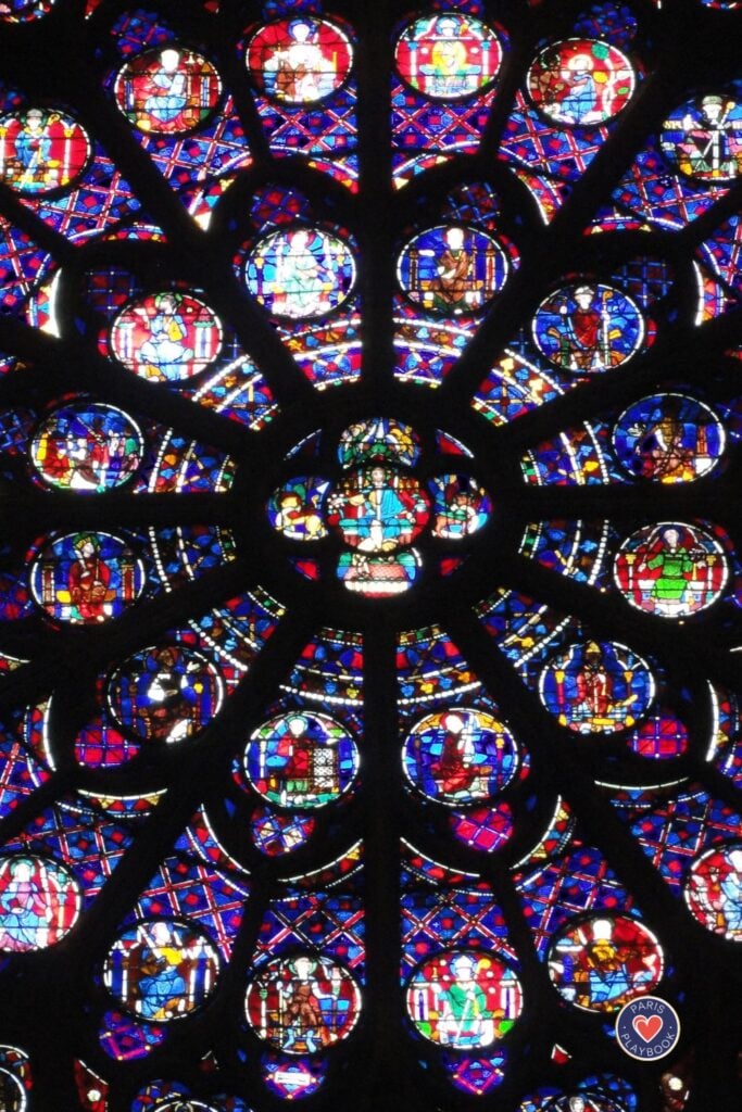 Ornate circular rose window of Sainte-Chapelle with intricate stained glass featuring biblical scenes in vibrant blues, reds, and golds with detailed stonework tracery