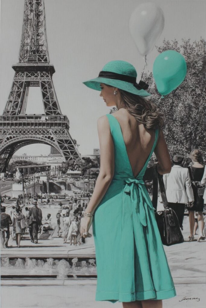 Black and white photograph with selective color showing woman in turquoise dress and hat holding balloon near Eiffel Tower